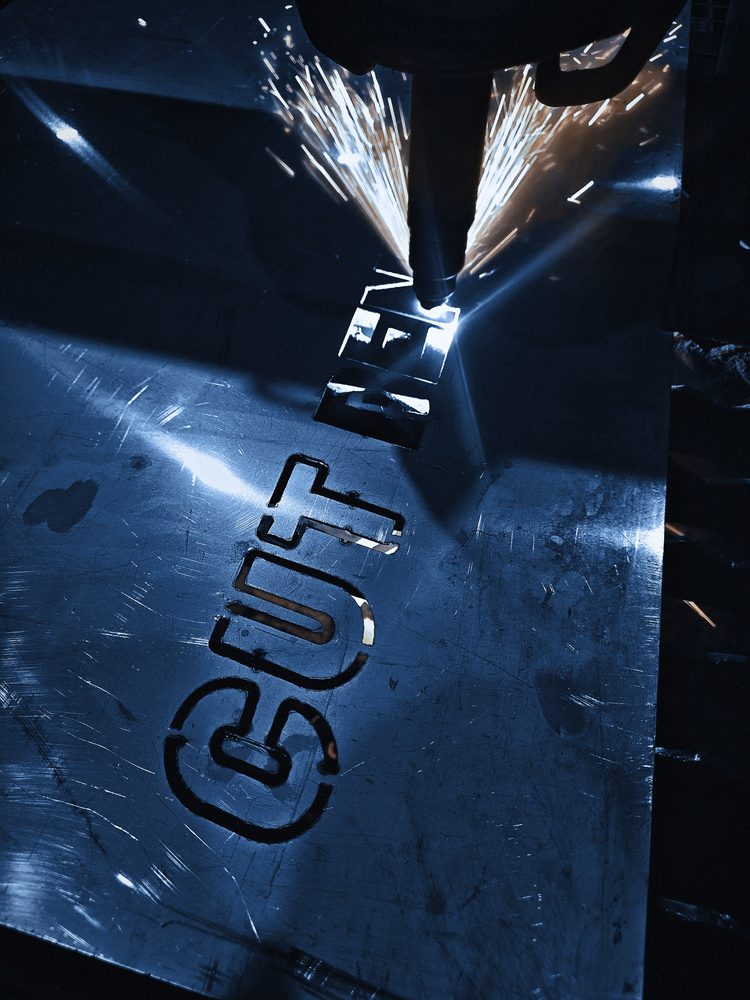The plasma torch cuts the Cut Bend Weld Go stencil out of thin steel sheet, sparks flying