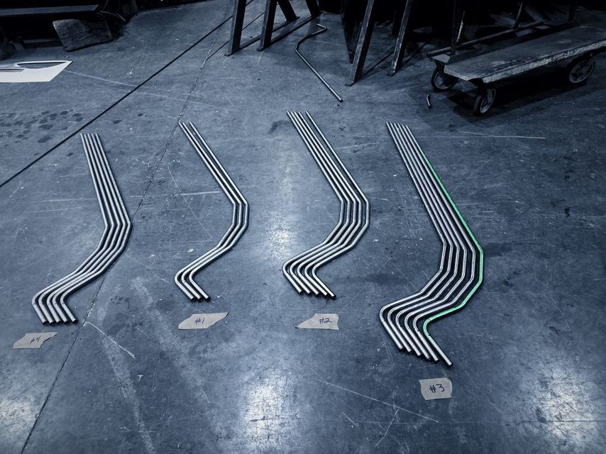Four sets of thin bent stainless tubes laid out on the shop floor