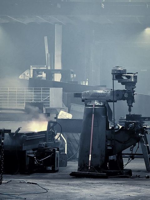 A milling machine stands in a hazy shop with sparks glowing behind it