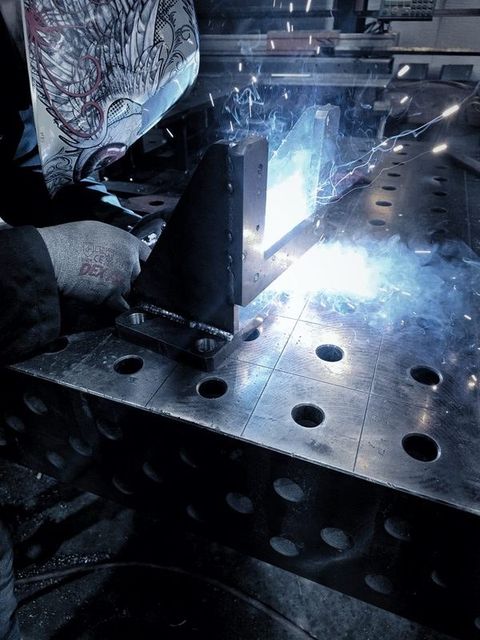 A welding arc lights up a part clamped to the fixture table