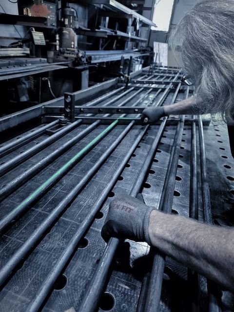 A man with white hair sets round bars into a rail on the fixture table